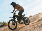 Person riding a dirt bike on a sandy trail with a clear sky.