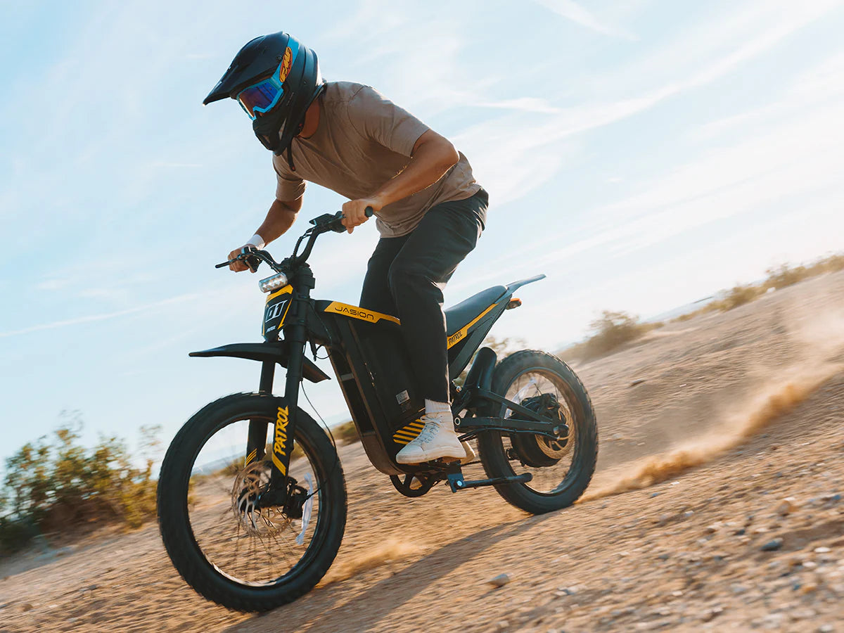 Person riding a dirt bike on a sandy trail with a clear sky.